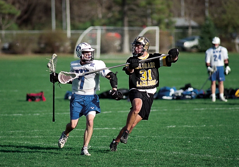 Two men running across a field with lacrosse sticks.