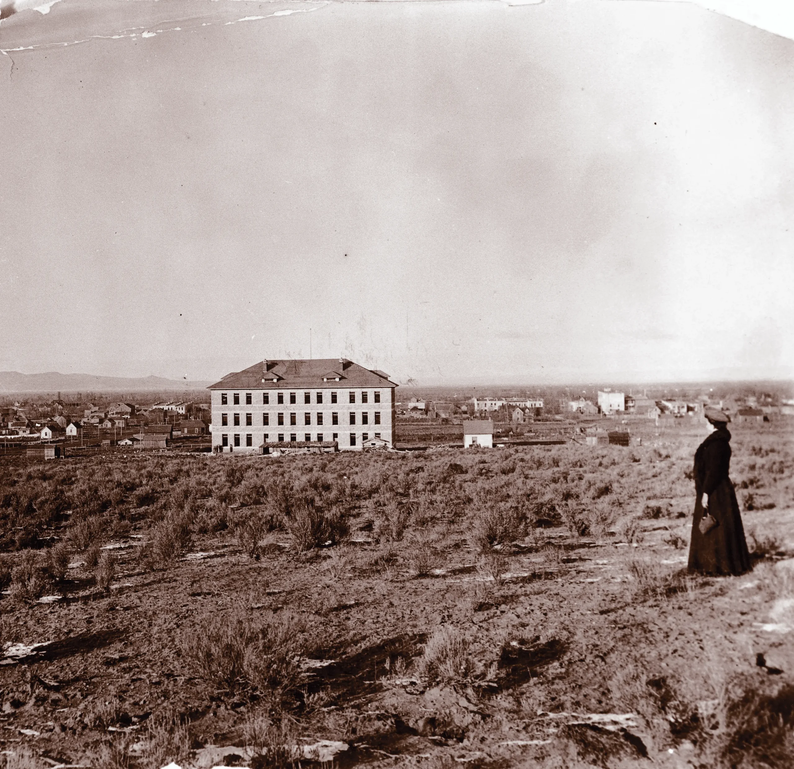 Historic black-and-white photograph of the Spori Building standing on a sparsely developed hillside in Rexburg, Idaho, with scattered homes and farmland in the distance.