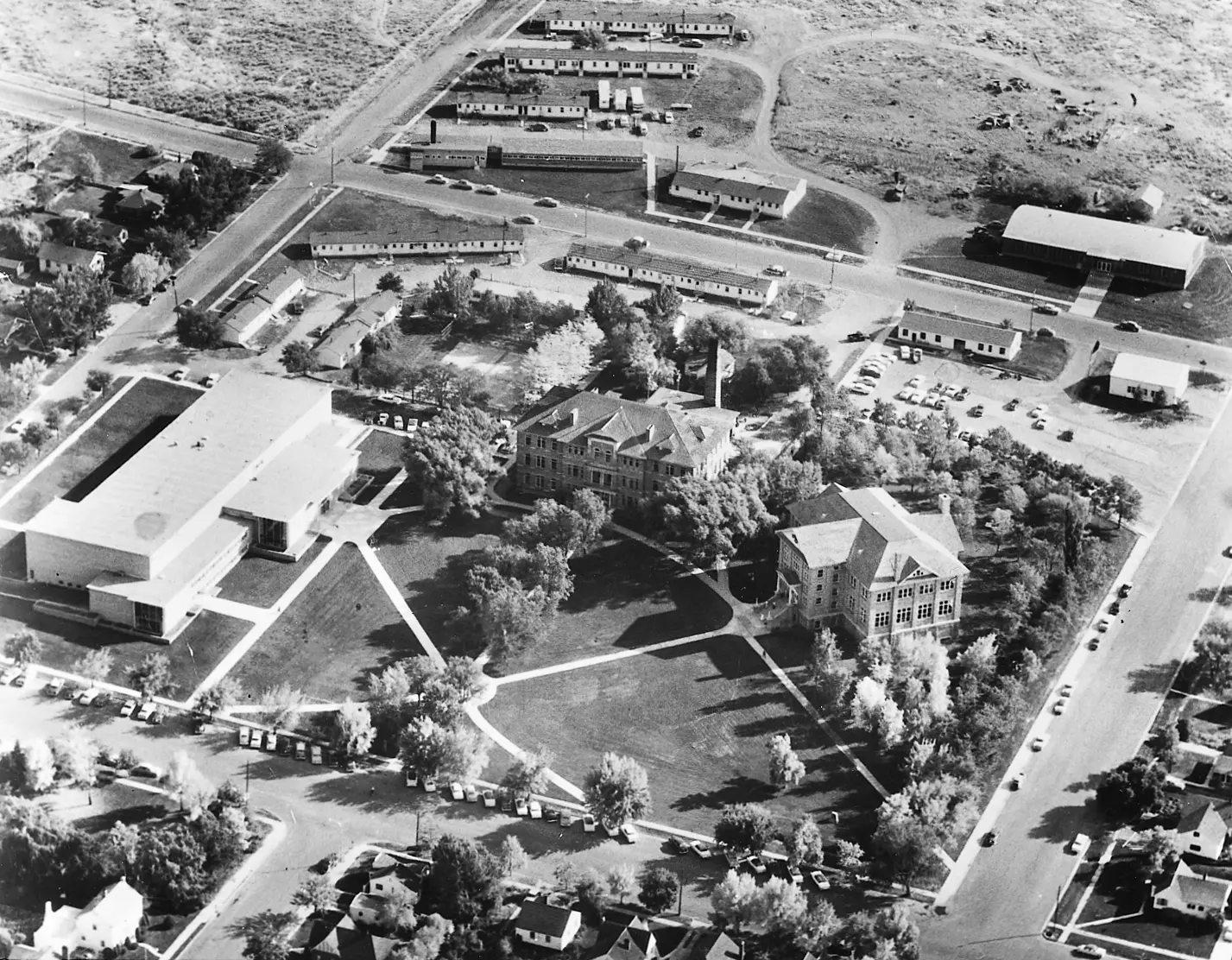 Black-and-white aerial photograph of the Ricks College campus, showing several academic buildings, lawns, paths, roads, and surrounding undeveloped land.