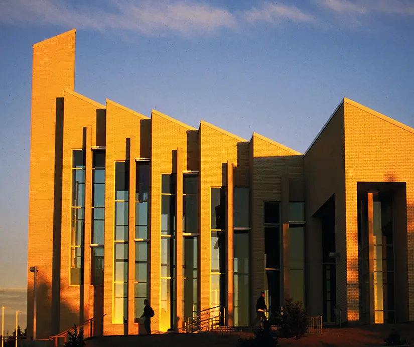 Modern BYU–Idaho academic building illuminated by warm late-day sunlight, with tall vertical windows and angular exterior walls.