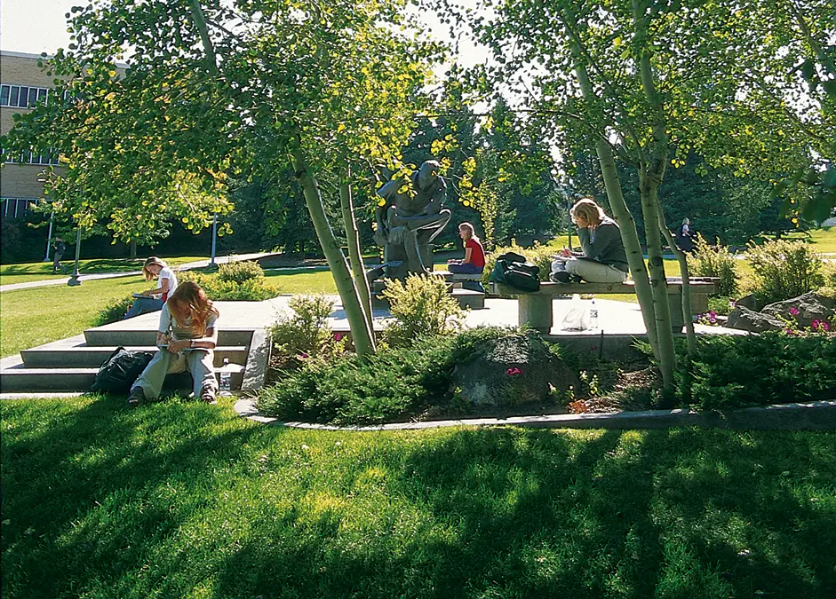 Students sit and talk among trees, lawns, flower beds, and benches in a landscaped garden on the BYU–Idaho campus.