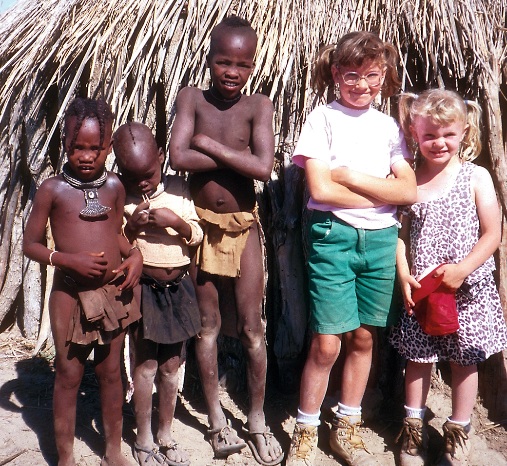 Three Himba children and Crandall's two daughters pose outside a thatched hut.