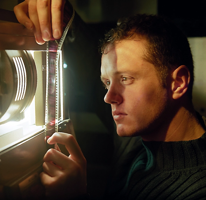 Ryan Isom works to feed a roll of film into a projector.