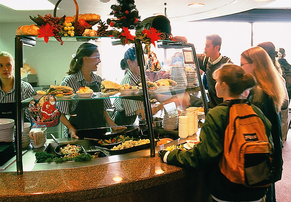 Students stand in line in front of a lunch counter where workers are serving food.