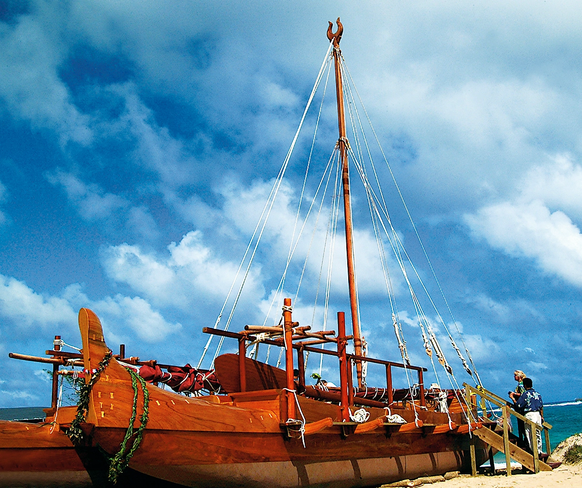 A large, wooden double-hulled canoe sitting on a beach.