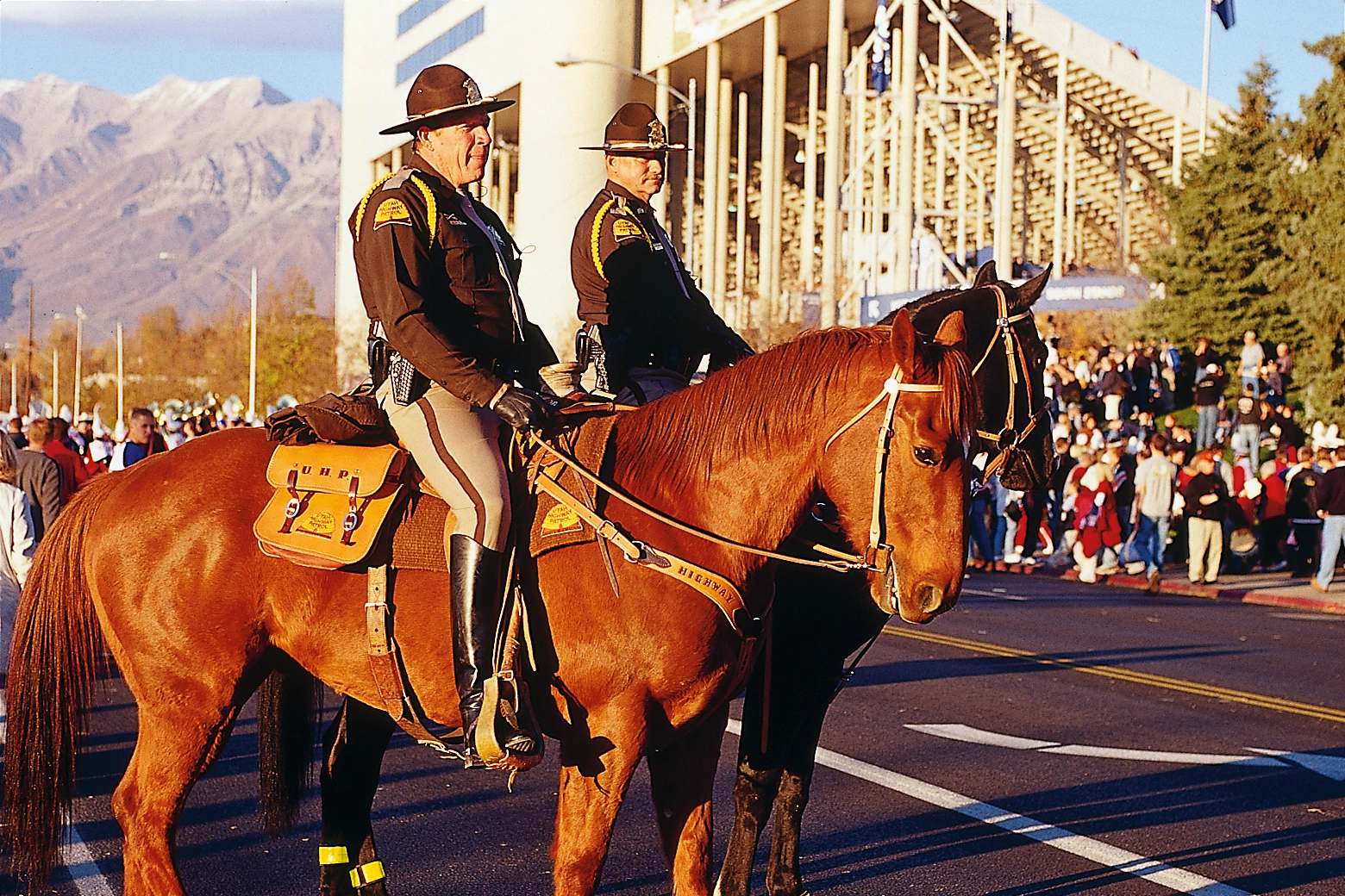 Two men in high way patrol uniforms sit on horses in front of the BYU stadium.