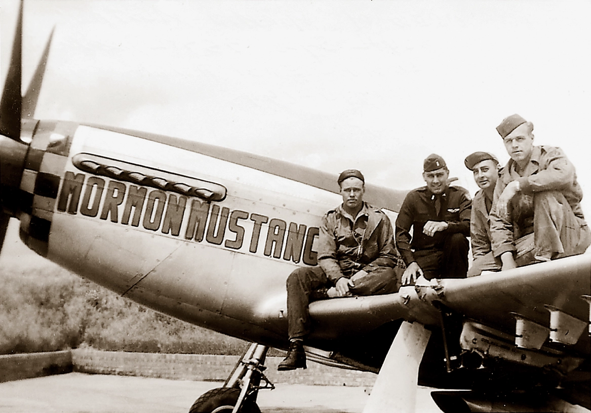 Four World War II pilots sit on the wing of a fighter plane that has the name "Mormon Mustang" painted on the side.