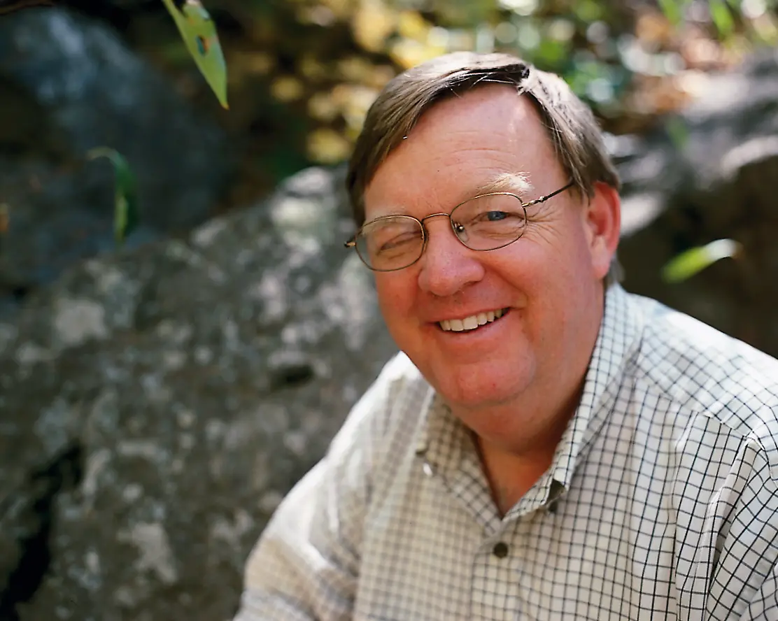 Portrait of BYU biology professor Larry St. Clair smiling outdoors beside a lichen-covered rock.