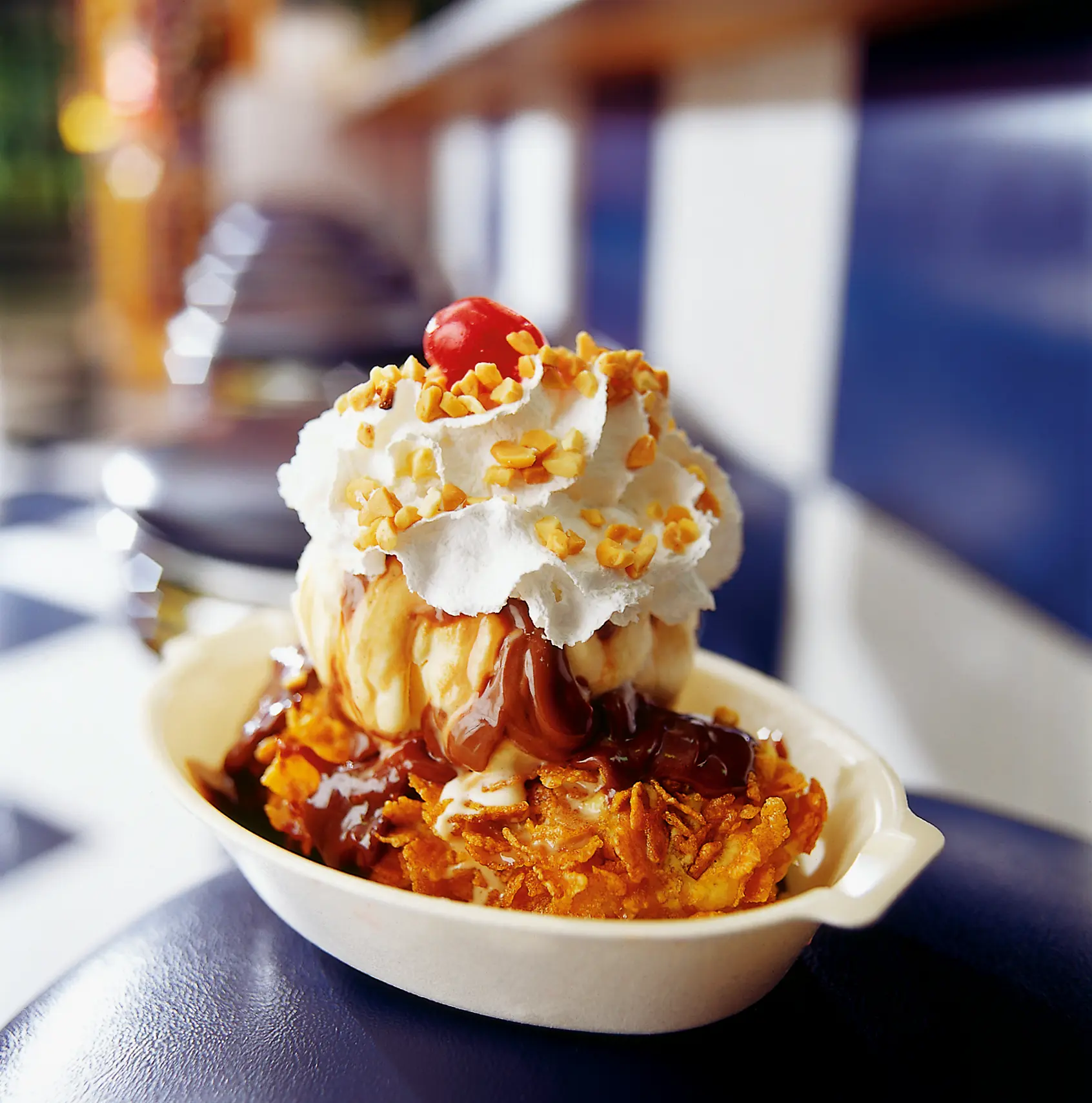 Deep-fried Milky Way bar sundae topped with scoops of ice cream, chocolate sauce, whipped cream, chopped nuts, and a cherry in a white bowl.