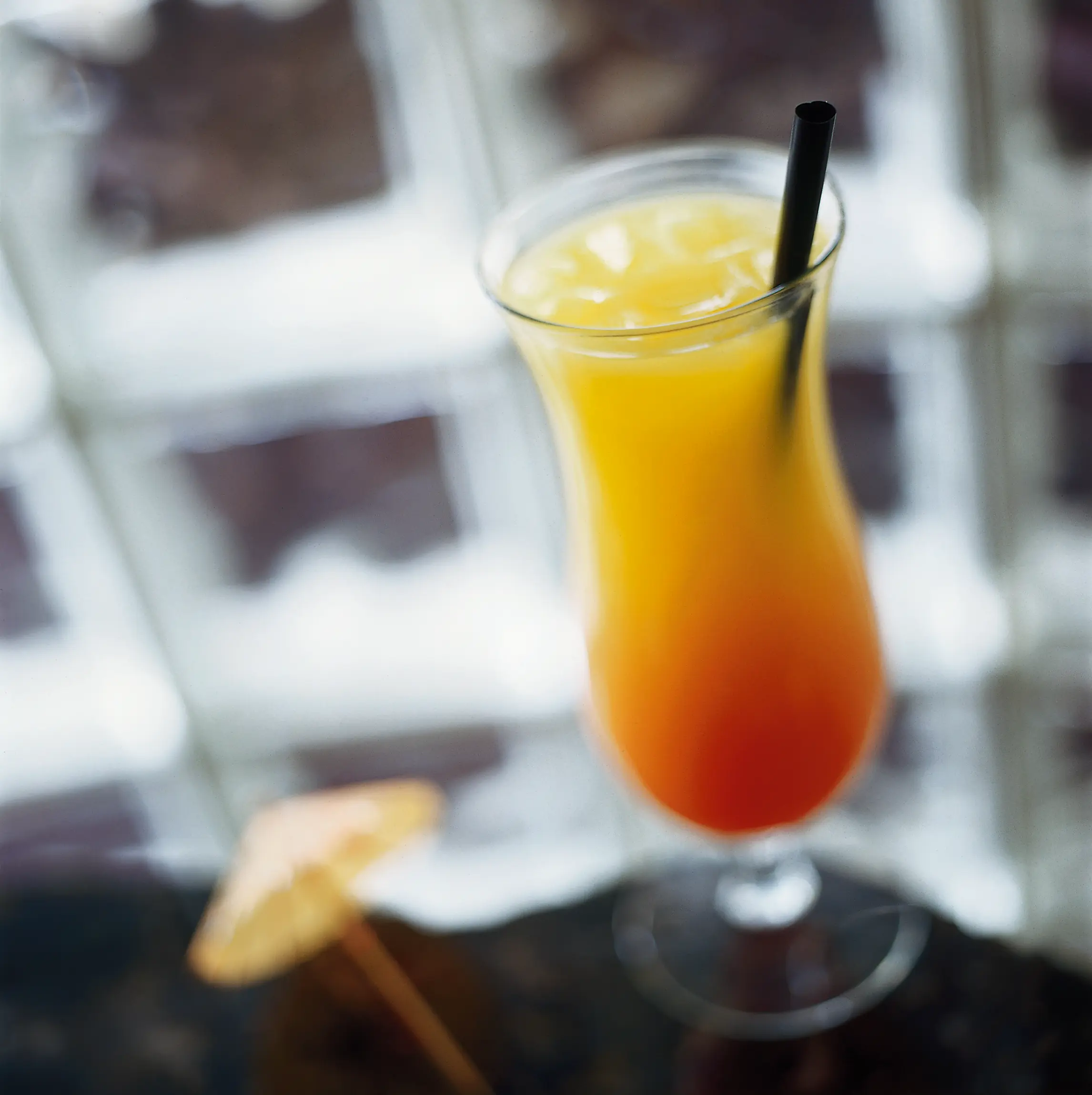 Tall glass of the Skyroom’s High in the Sky specialty drink, layered from deep red at the bottom to orange and yellow at the top, with a black straw.