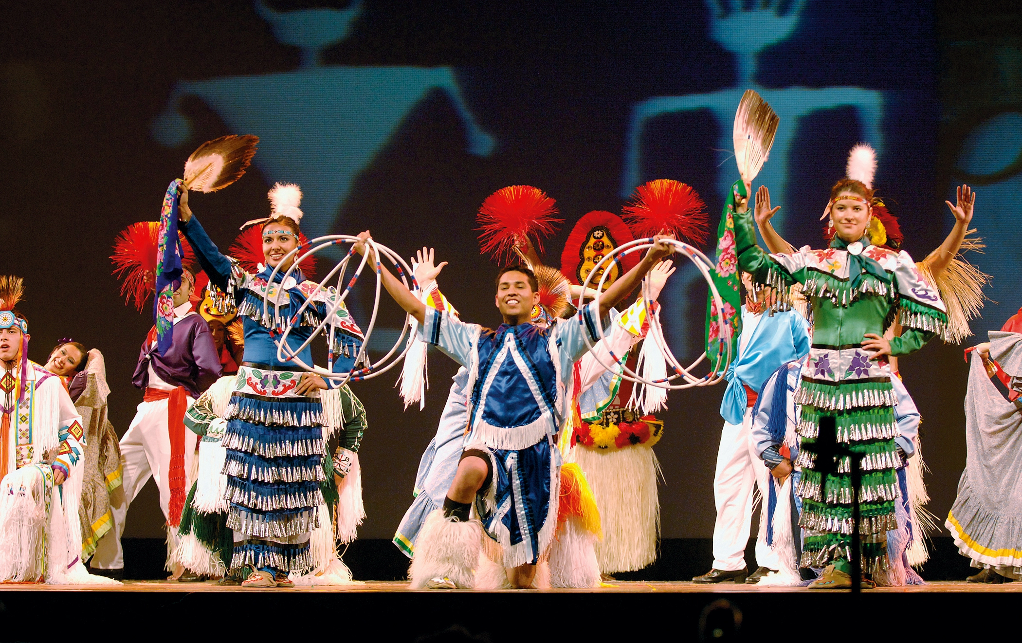 A group of performers wearing traditional Native American dress.