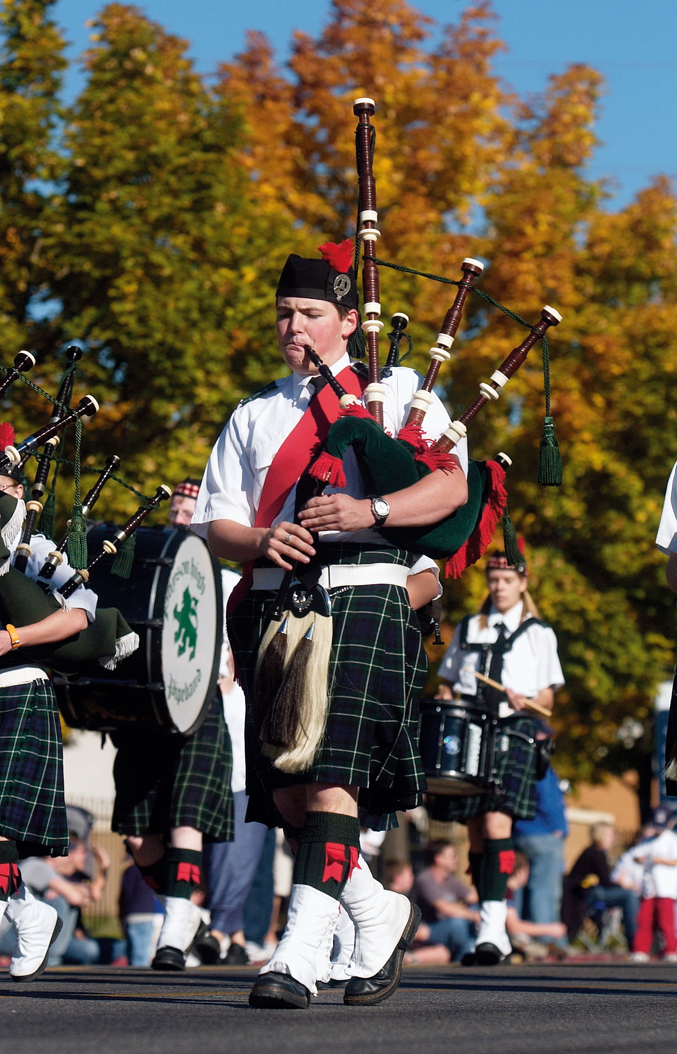 A man wearing a kilt walks down a street while playing the bagpipes.