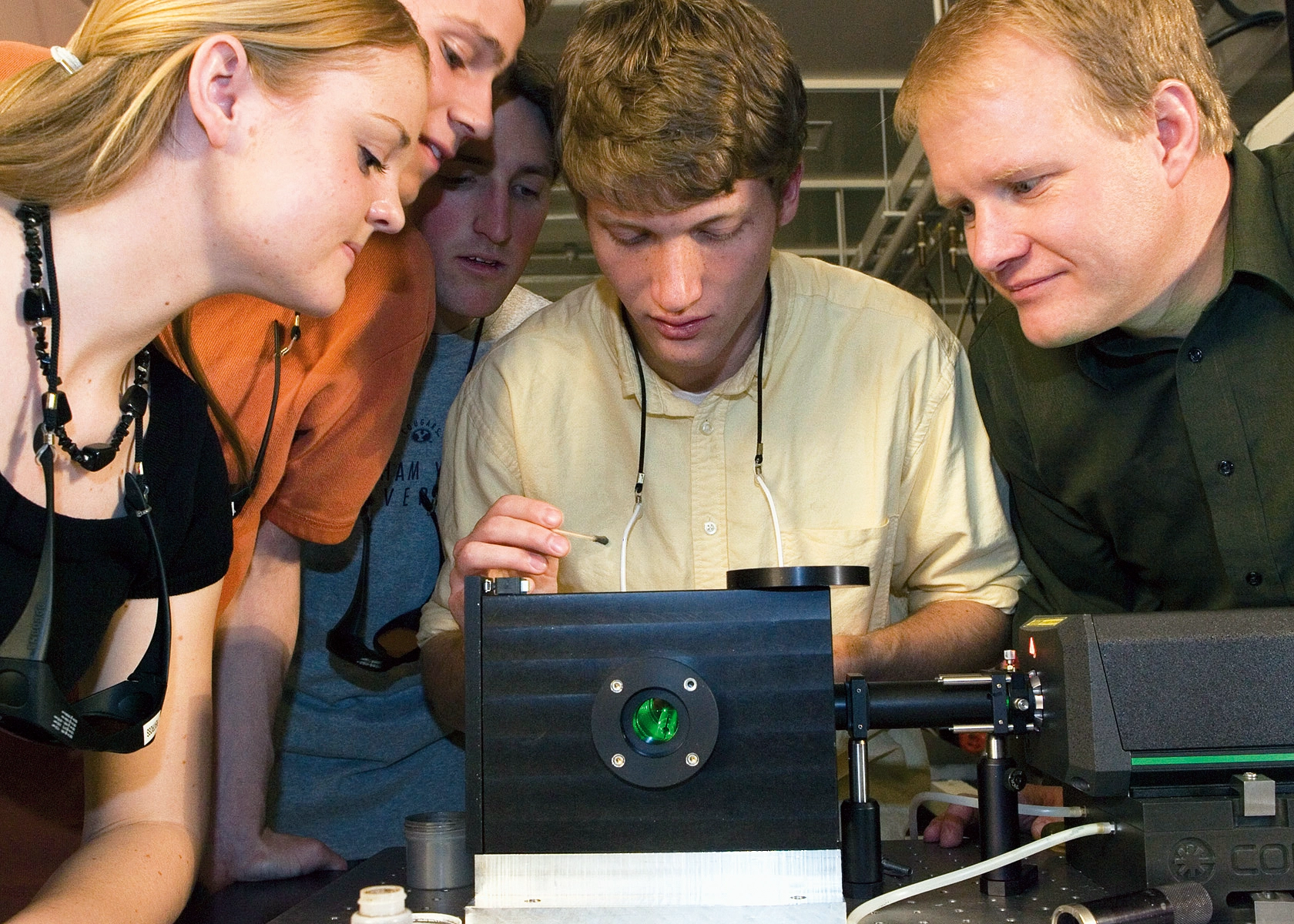 A group of students stand around a laser.