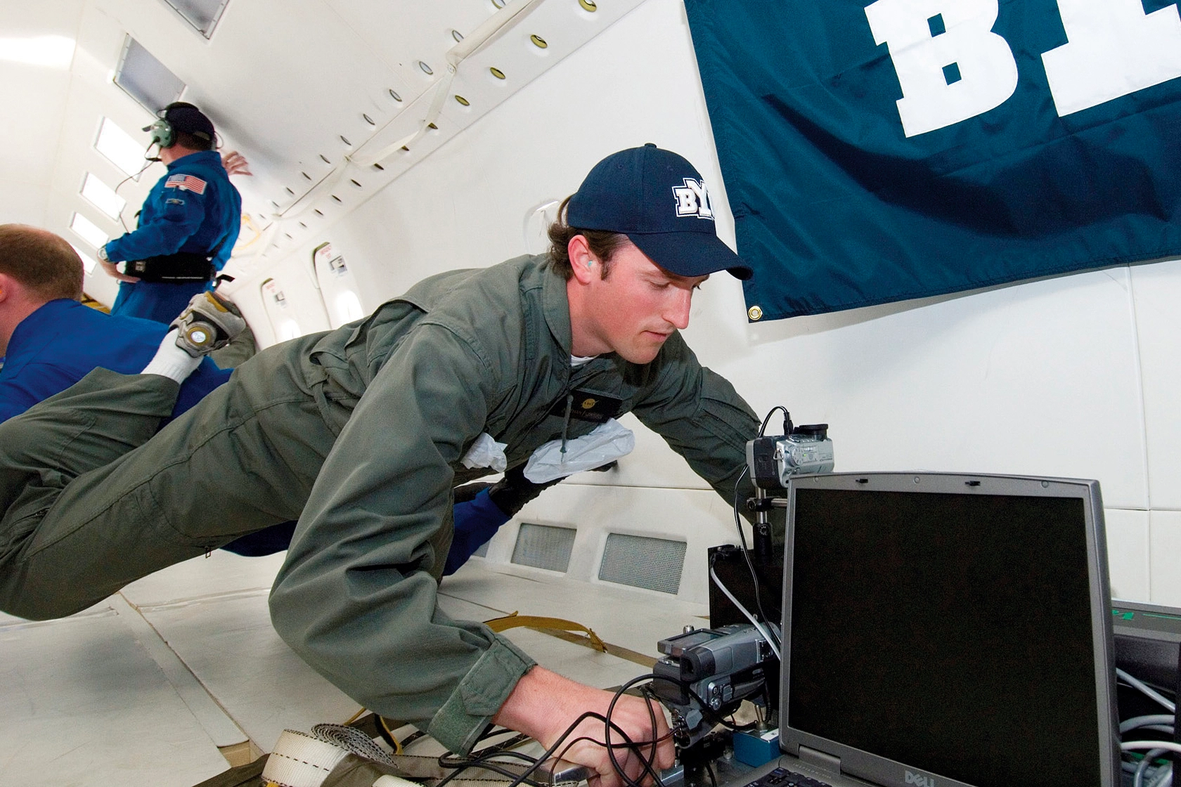 Nathan powers floats in front of computer equipment while wearing a BYU hat.