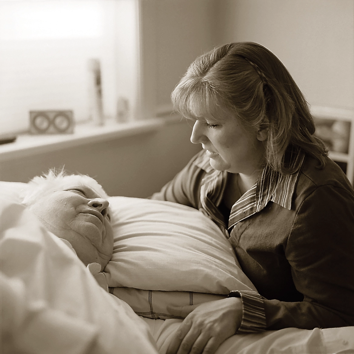 A woman sits by the bed of an elderly woman.