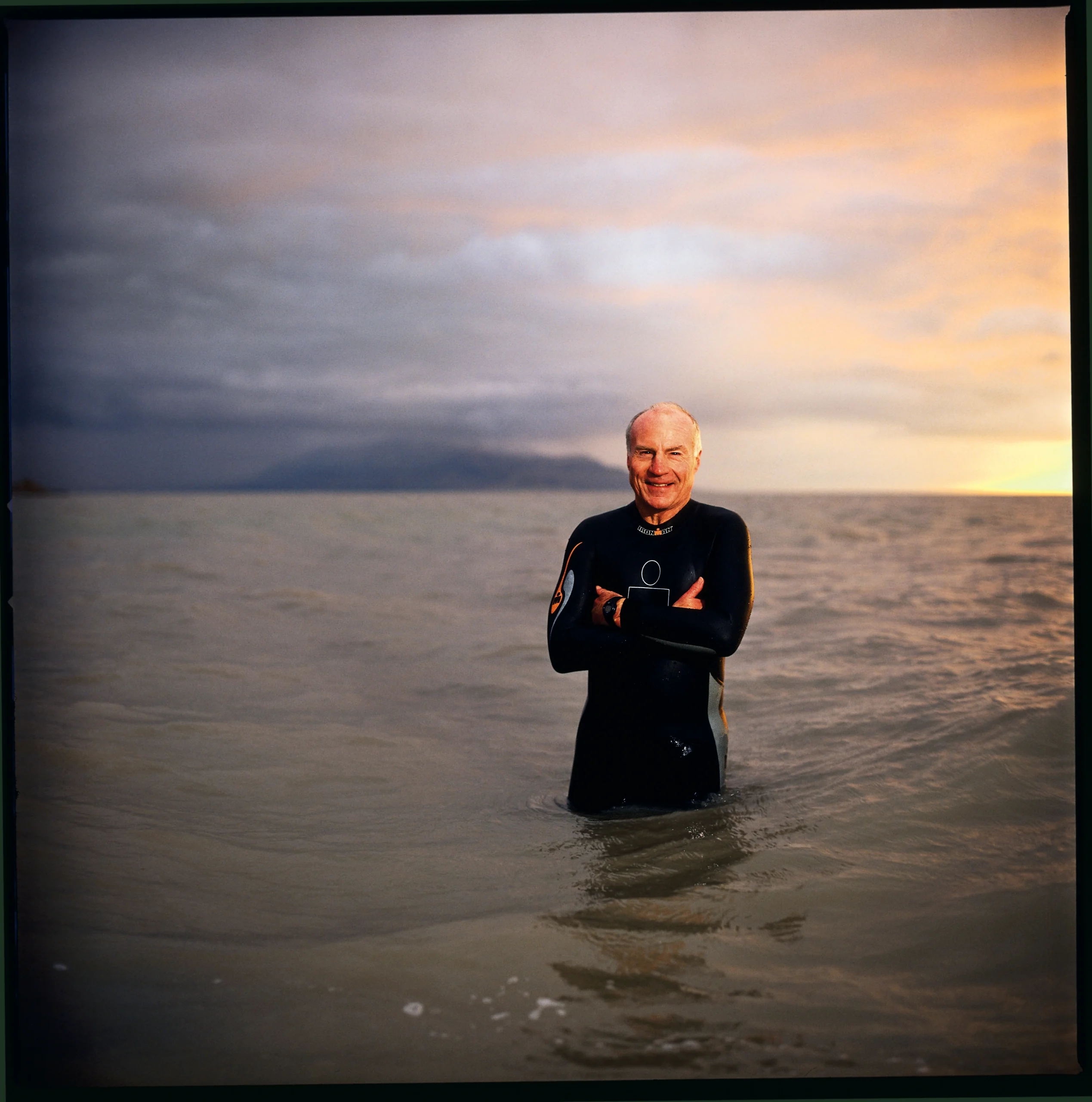 James V. Hansen stands with his arms crossed while wearing a wetsuit in a lake.