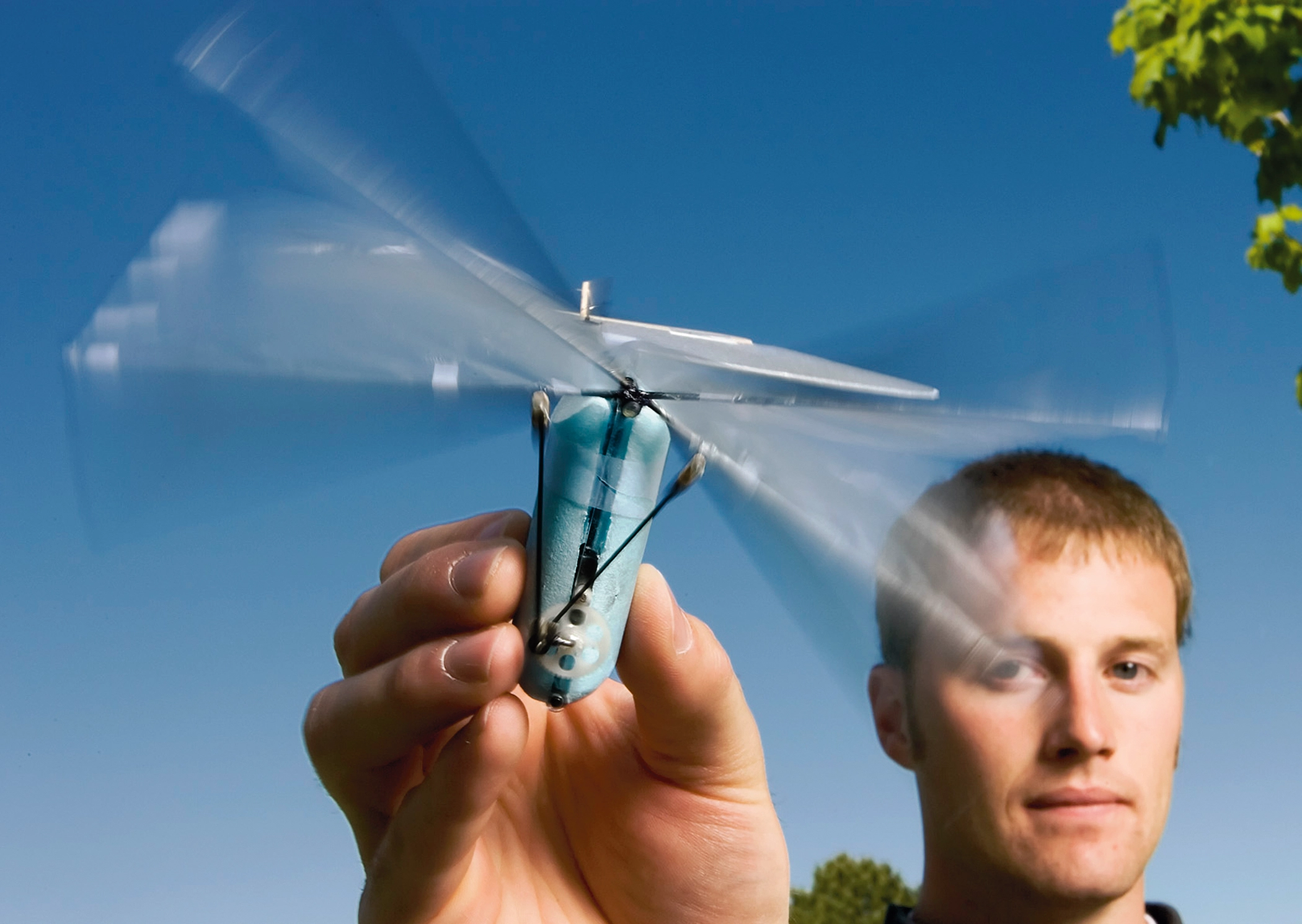 A man holding a contraption with a small, bulbous body and wings on top that are blurred from being in motion.
