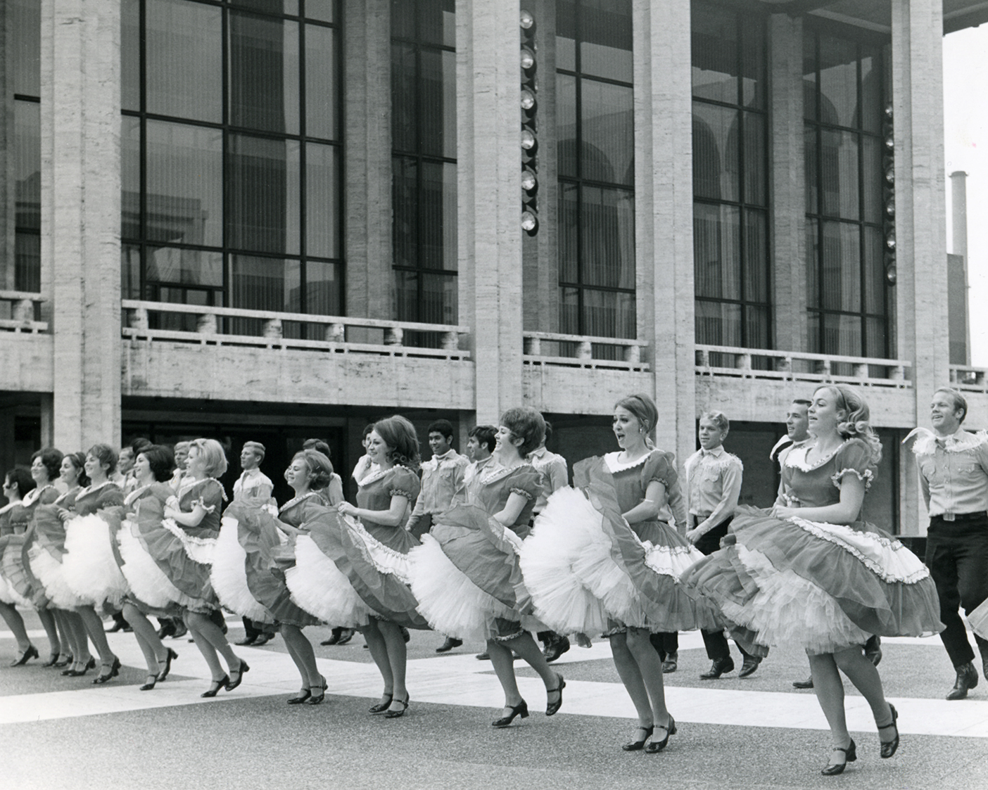 BYU folk dancers dance on broadway street in this black and white image from the 1970s.