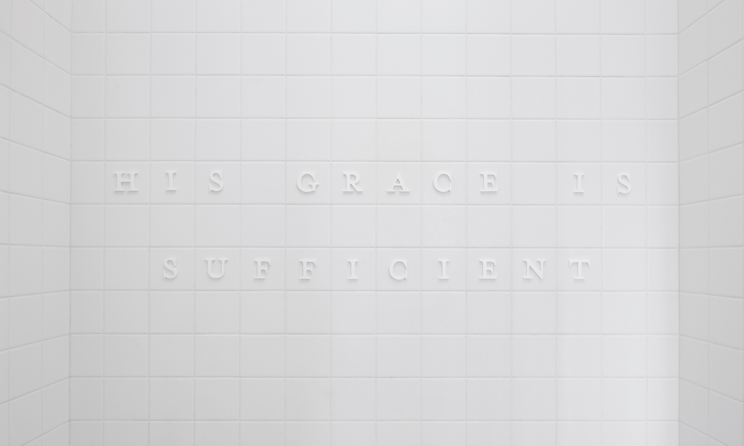 A white tile wall that reads "His grace is sufficient."