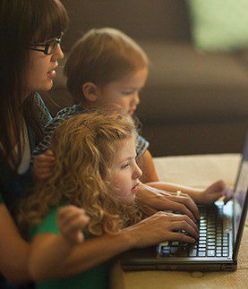 A mother blogging, with two young children on her lap.