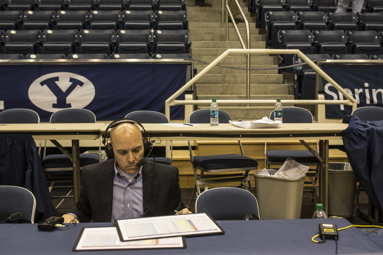 Greg Wrubell at his table on the sidelines of the basketball court with a headset on.