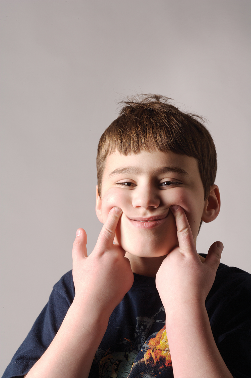 A young boy using his pointer fingers to shape his mouth into a smile.