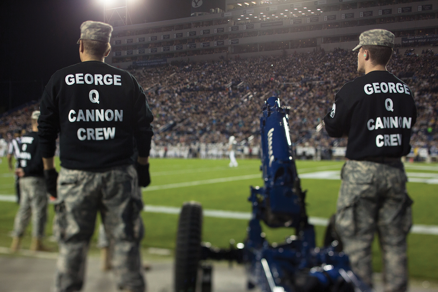 ROTC members stand beside a cannon on the field.