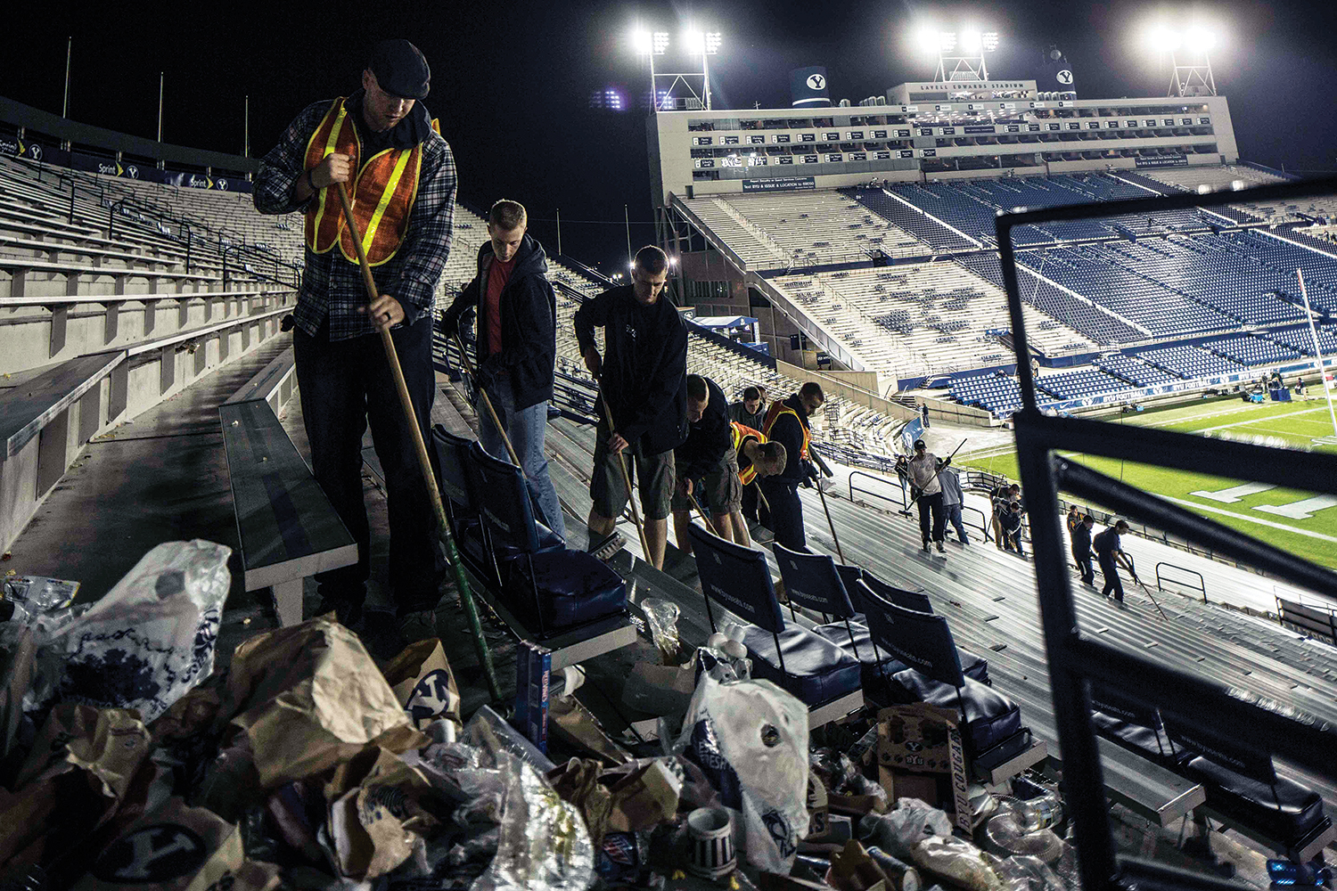 After collecting recyclables, crews sweep trash out of the aisles of the LaVell Edwards Stadium bleachers.