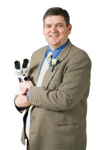 Nathan J. Cherrington is smiling and holding his microscope.