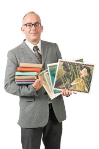 Brett Helquist is holding several books in one arm and showing some of his illustrations in his other hand.