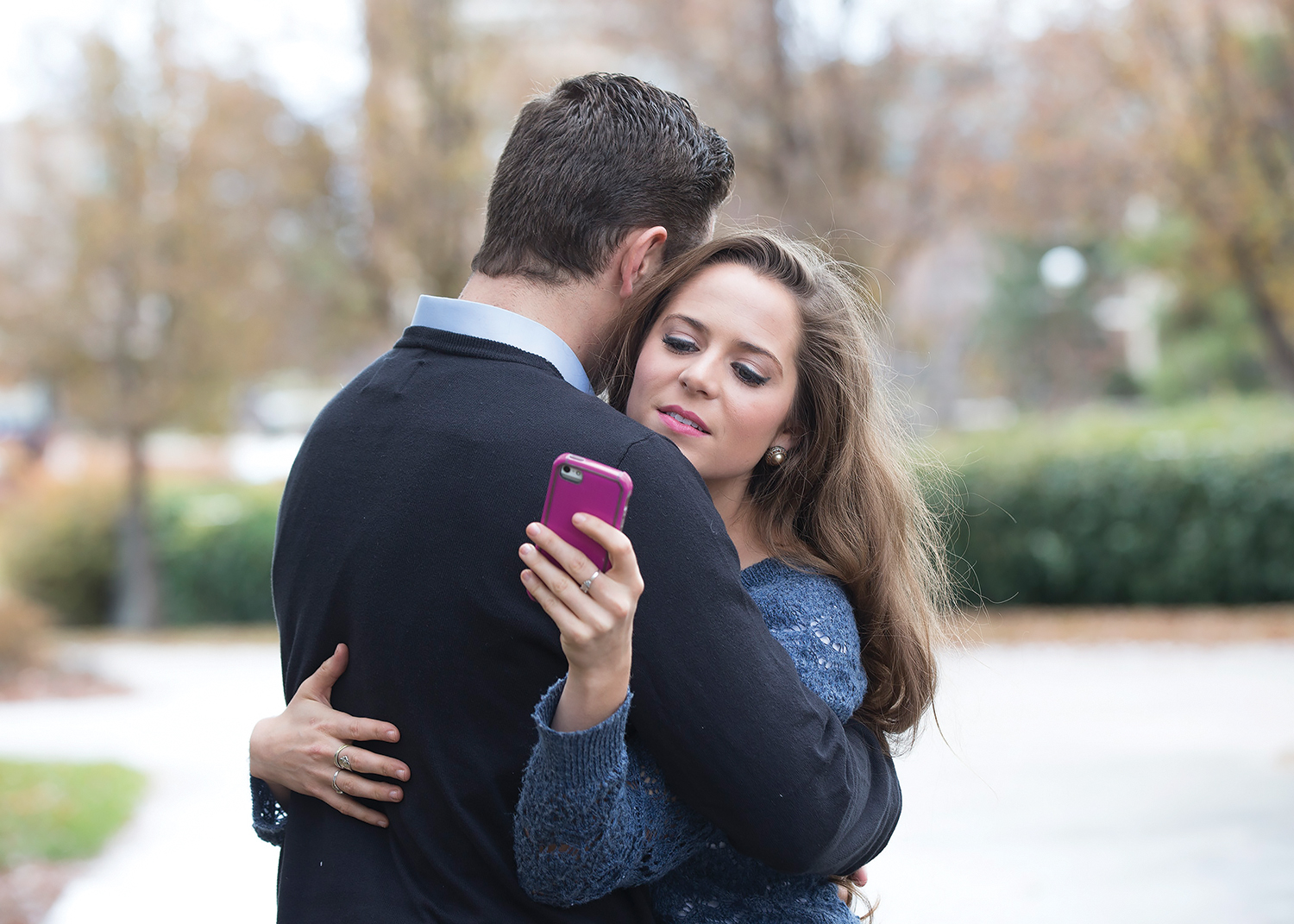 An embracing couple is distracted by cell phones.