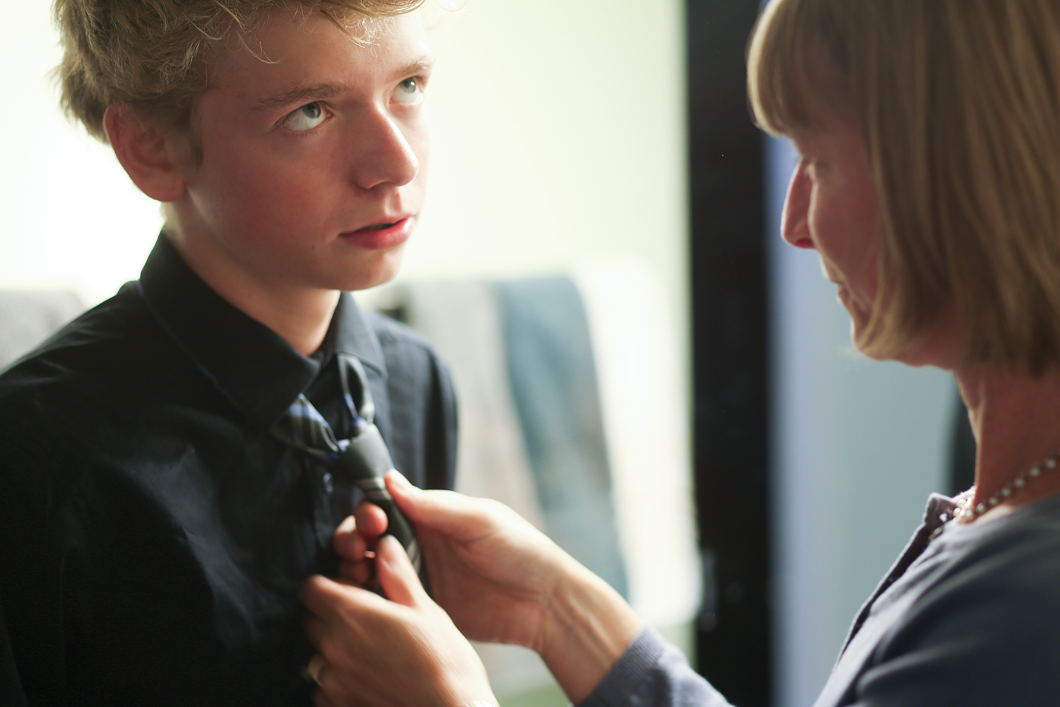 Young man rolling his eyes as his mother fixes his tie.