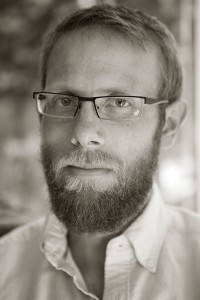 A bearded man with glasses and a serious face.