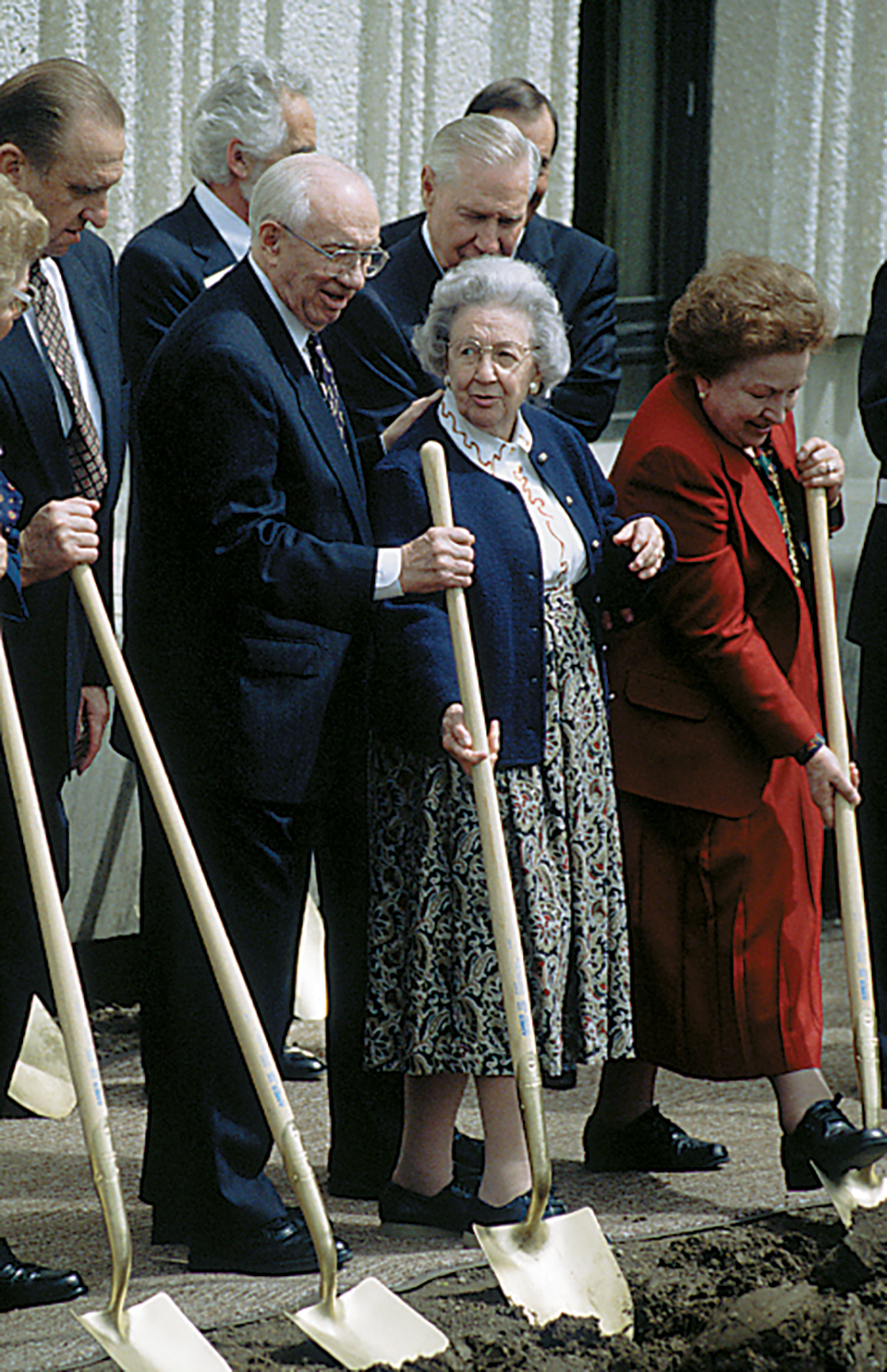Thomas S. Monson, Gordon B. Hinckley, and Majorie Pay Hinckley and others stand side by side holding their shovels in the dirt.