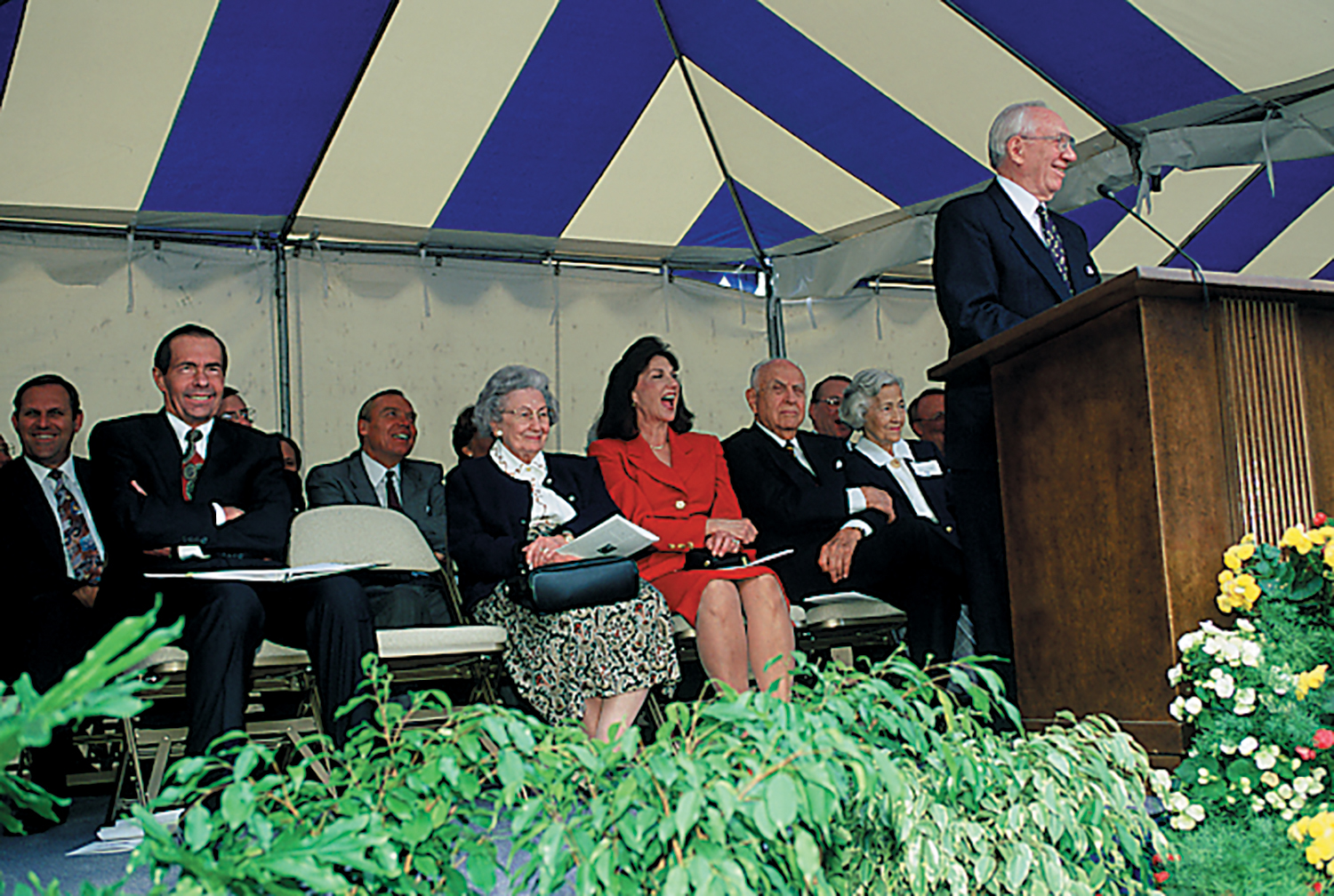 President Gordon B. Hinckley speaking at a podium with board members sitting behind him.