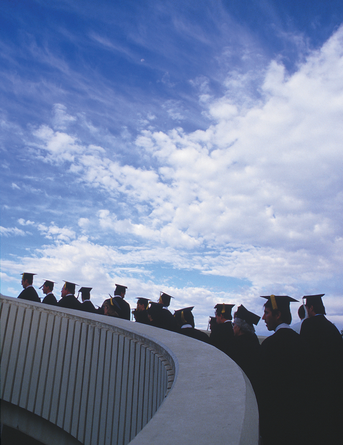 Students in their graduation robes walking up the spiral ramp on campus.