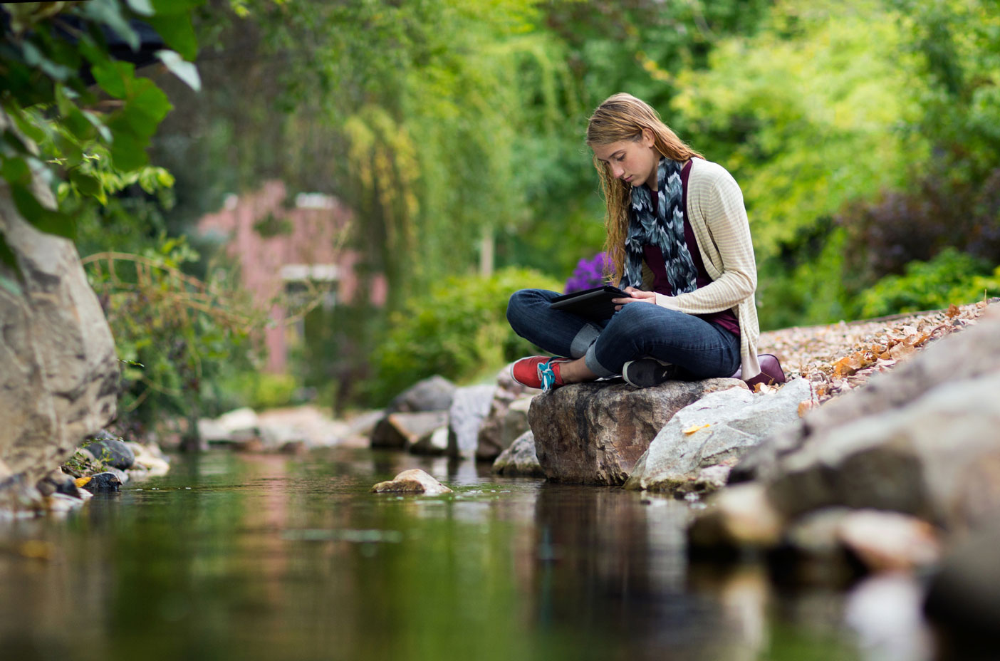 A student sits on a rock by a creek.