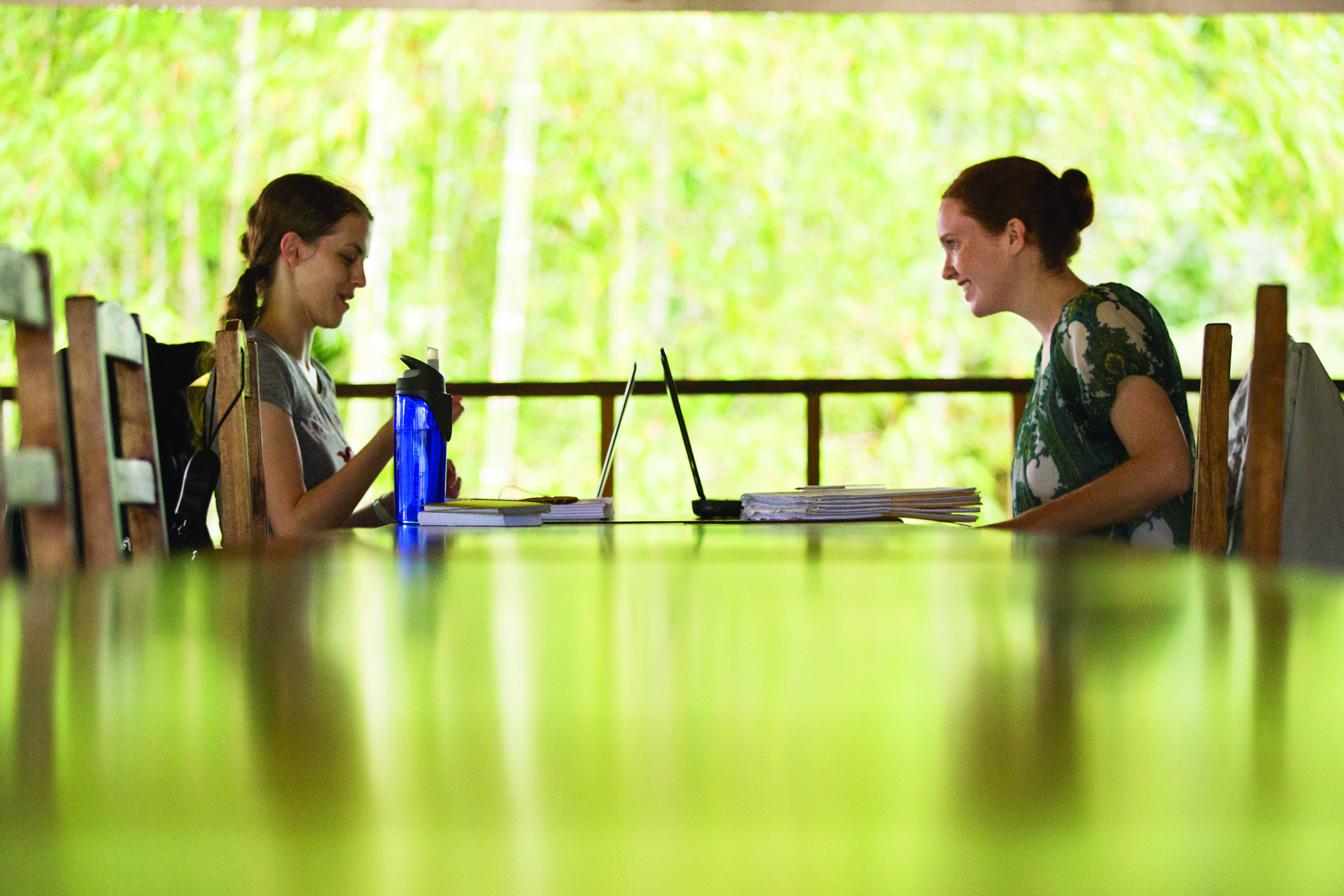 Two students work on their laptops in the open-air field school