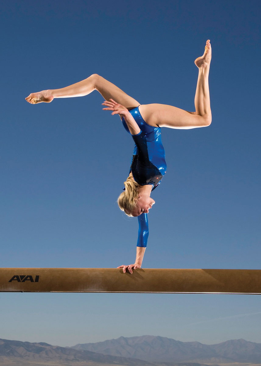 BYU gymnast balancing on one hand on a balance beam.