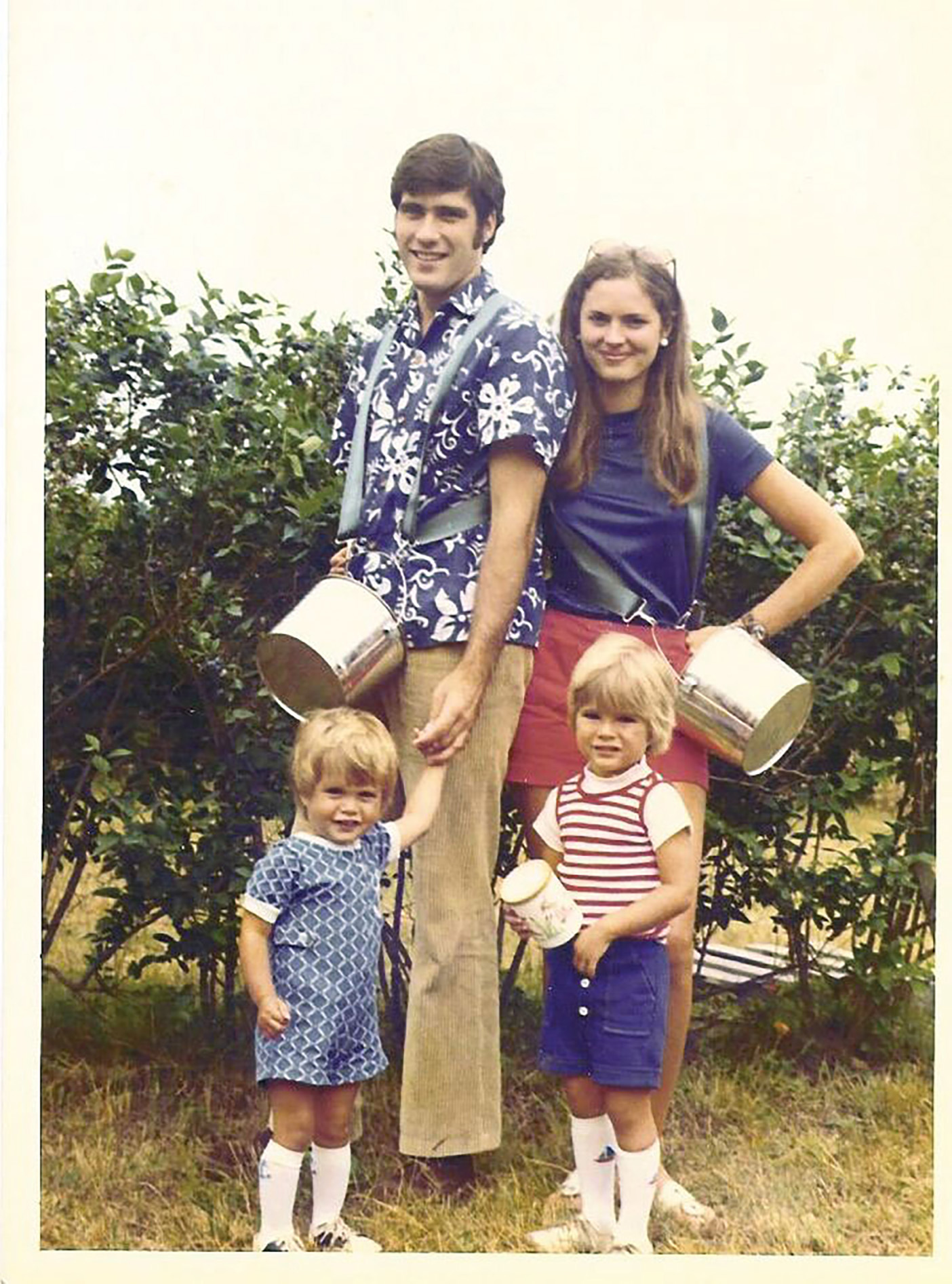 Ann and Mitt with two of their little boys, picking fruit in an orchard.