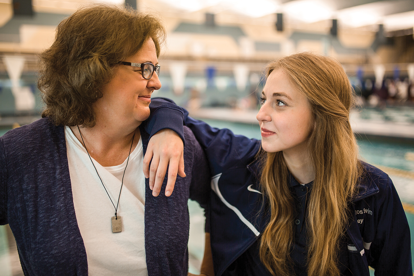 Daughter and mother lovingly look at one another in front of a pool.