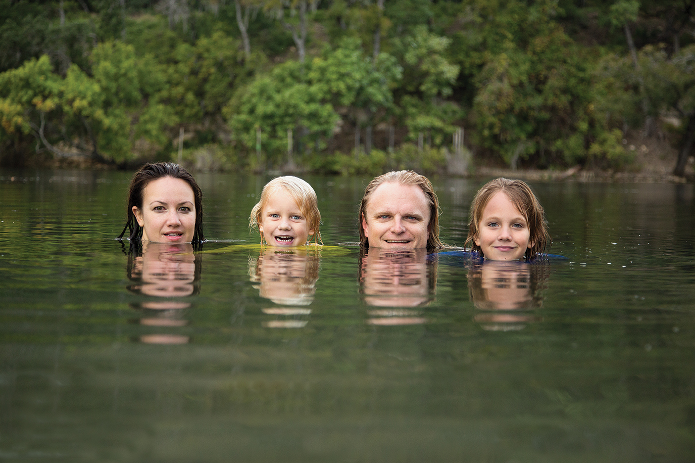 The Hanselman family, Lyndee, Fitz, Eagen, and Anders are floating in a lake with their heads poking out, smiling for a photo.