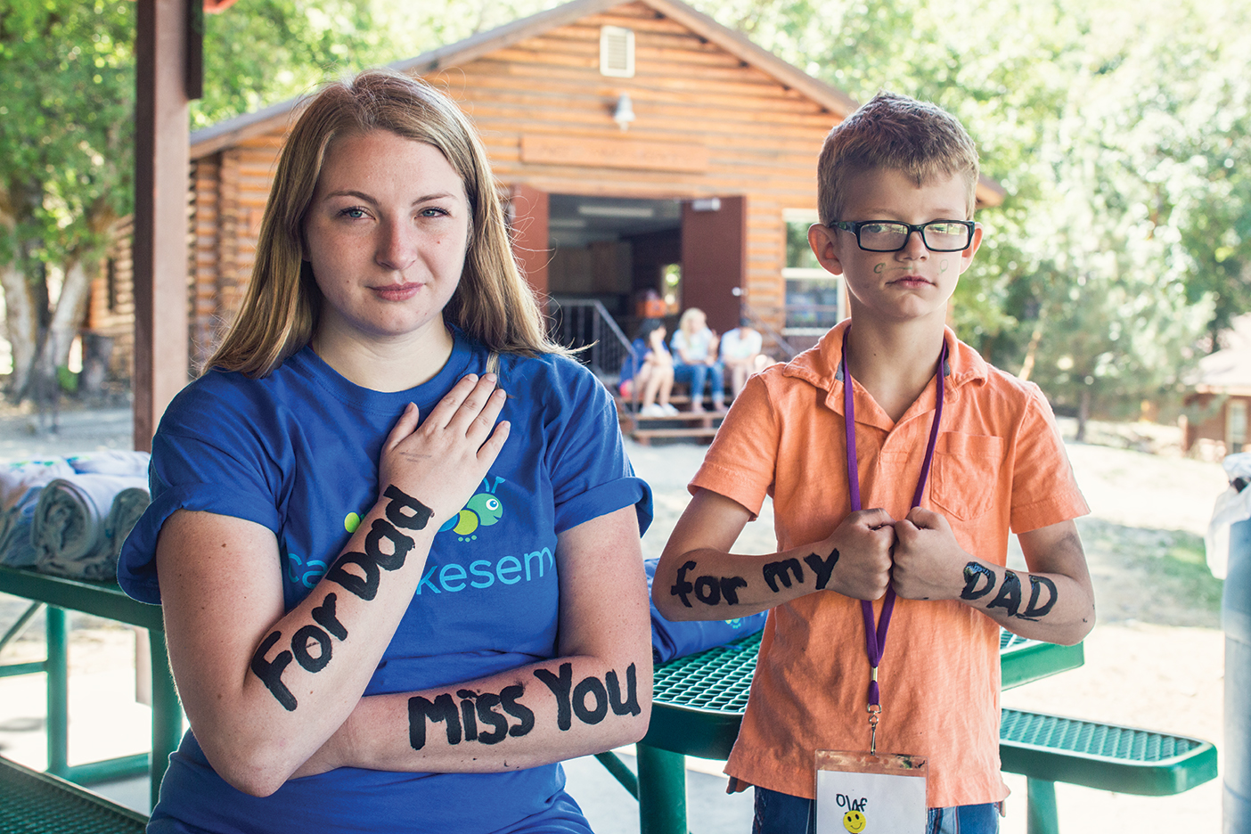 Michelle L. Mayer (&rsquo;20)—known as &ldquo;Smu&rdquo; here, where everyone goes by nicknames—poses for a picture with 8-year-old &ldquo;Wolverine.&rdquo; The words on their arms combine to read, &ldquo;For our dads.&rdquo; They smile for the camera then step away for a silent, tearful hug.