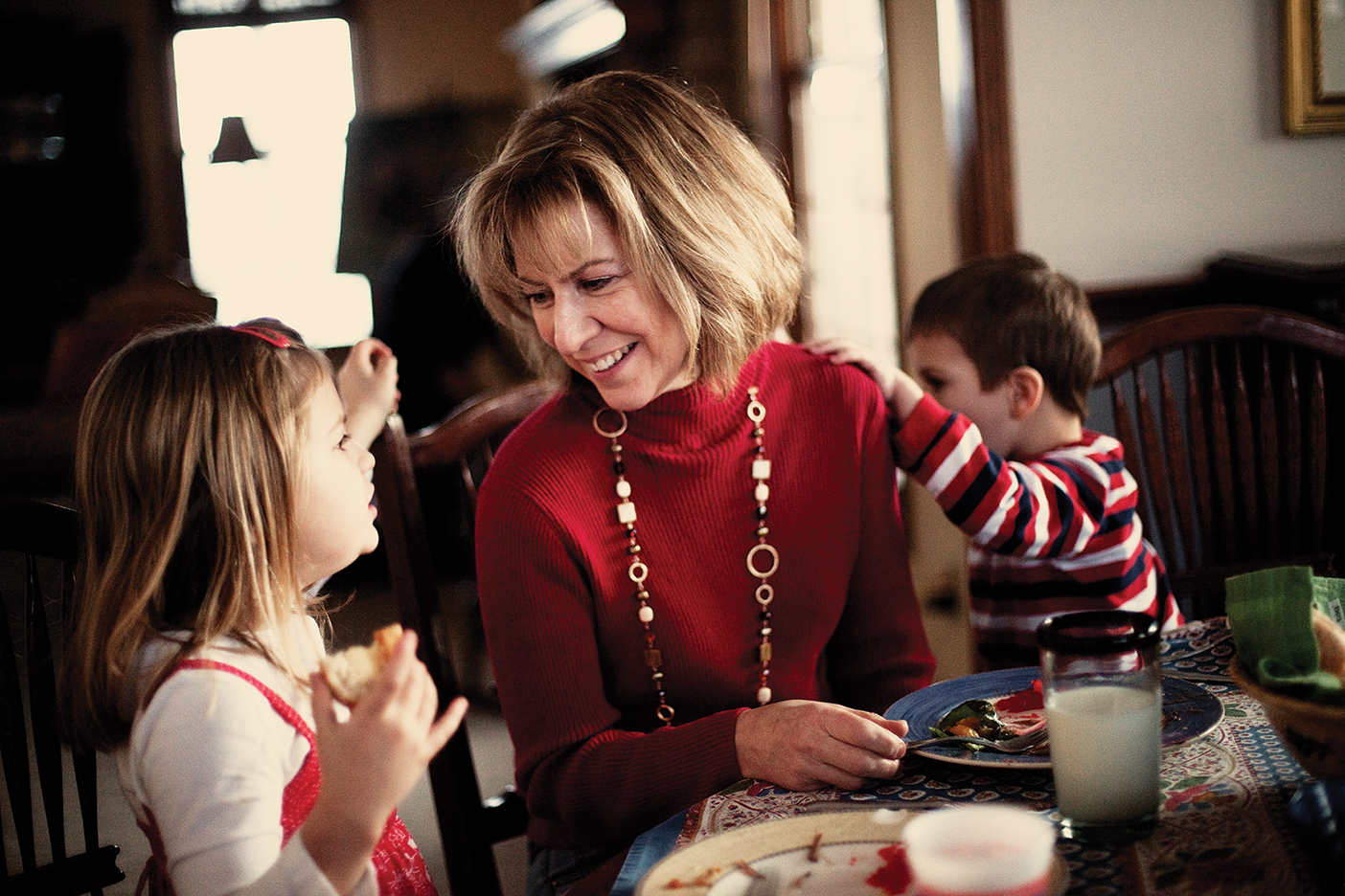 a mother smiles at her two children, a young girl and a young boy, at the dinner table