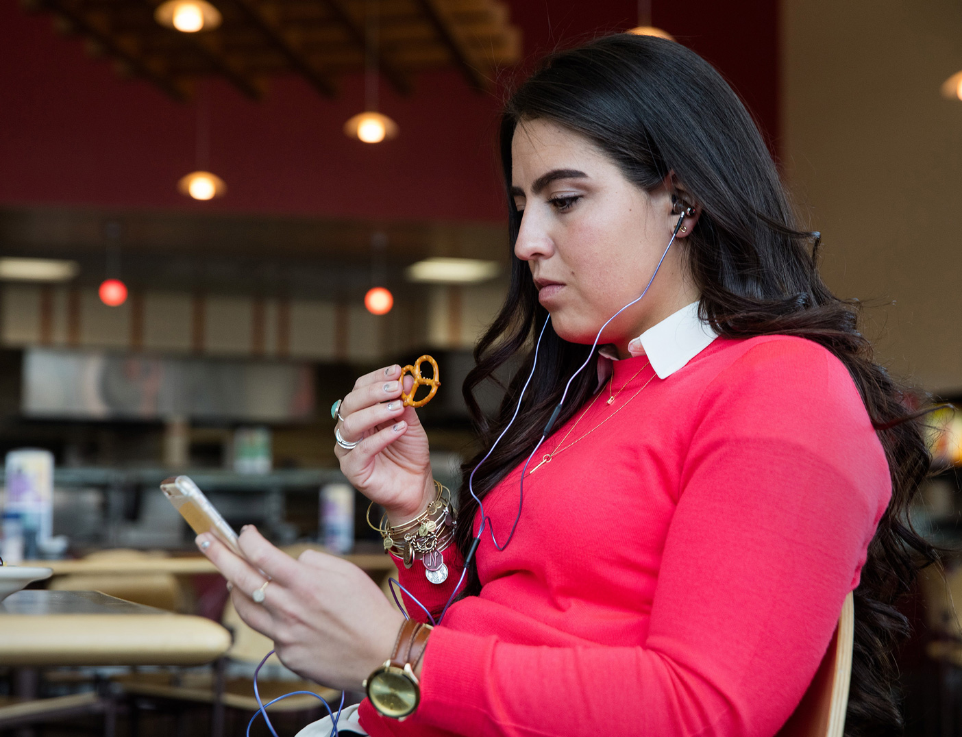 A woman eats a pretzel with her headphones blasting music.