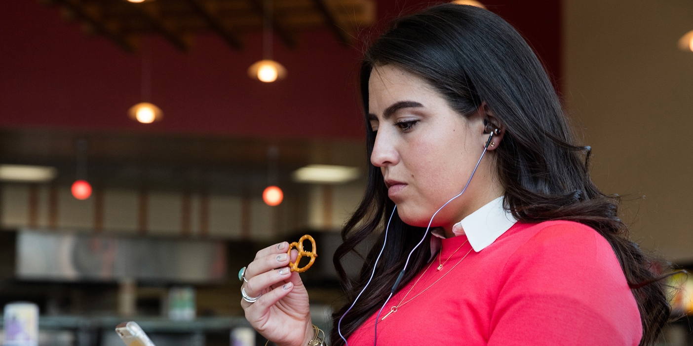 A woman eats a pretzel with her headphones blasting music.