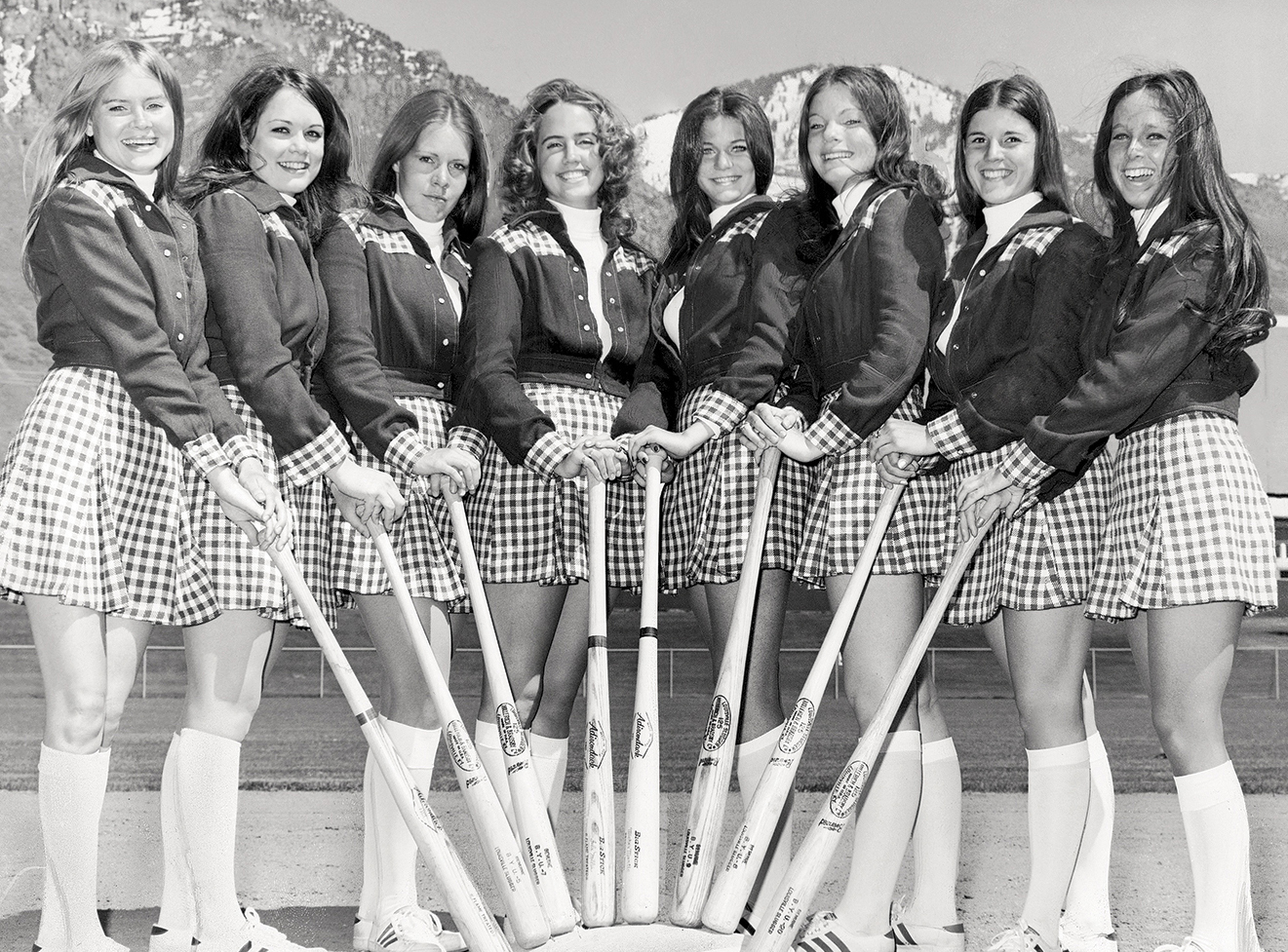 Eight BYU female students hold bats on the campus baseball diamond.