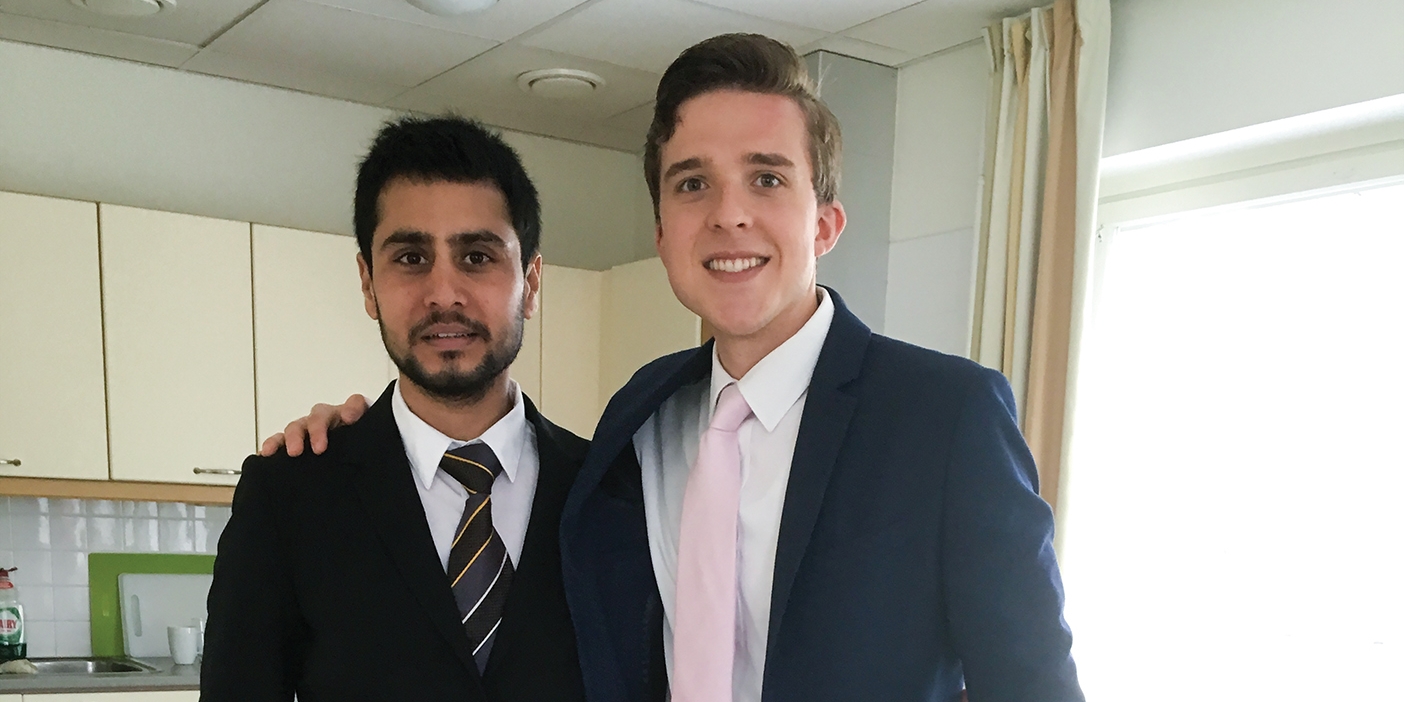 two men stand together and smile in suits