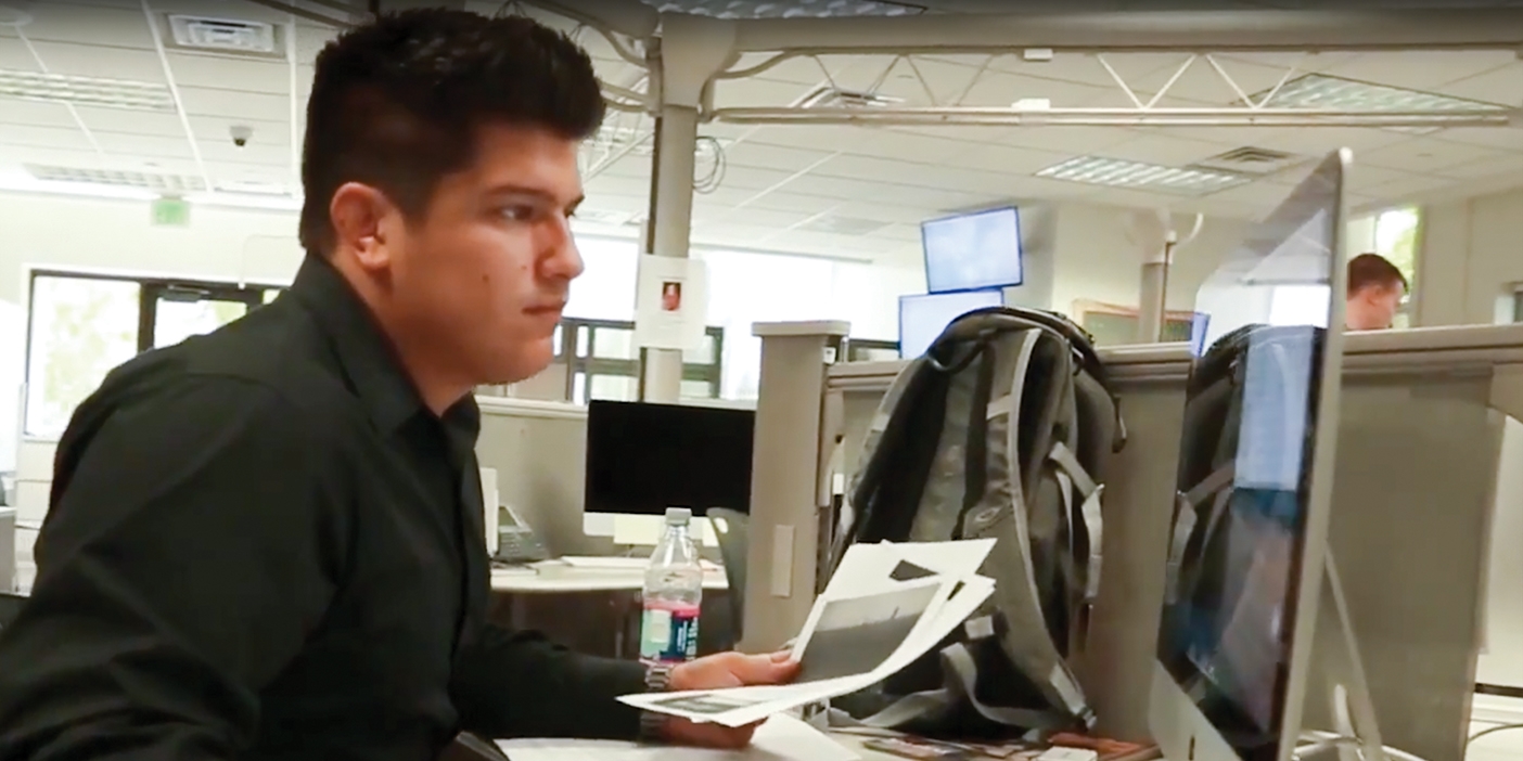 guy sits at news desk, working on computer