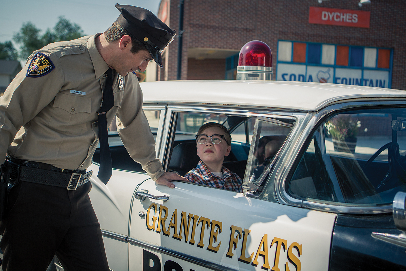 A boy inside of a patrol car is talked to by a policeman